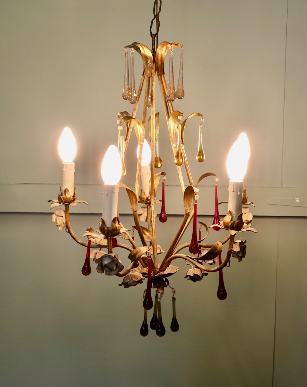 A French gilt metal chandelier featuring five curved candle arms decorated with leaf foliage and hung with clear, amber, and red glass teardrops. View IV