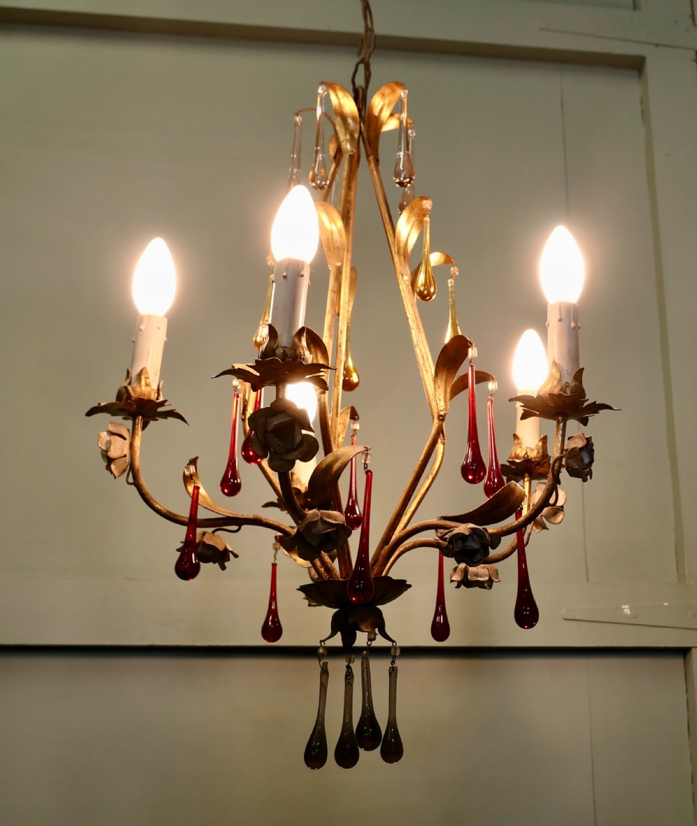 A French gilt metal chandelier featuring five curved candle arms decorated with leaf foliage and hung with clear, amber, and red glass teardrops. View VI