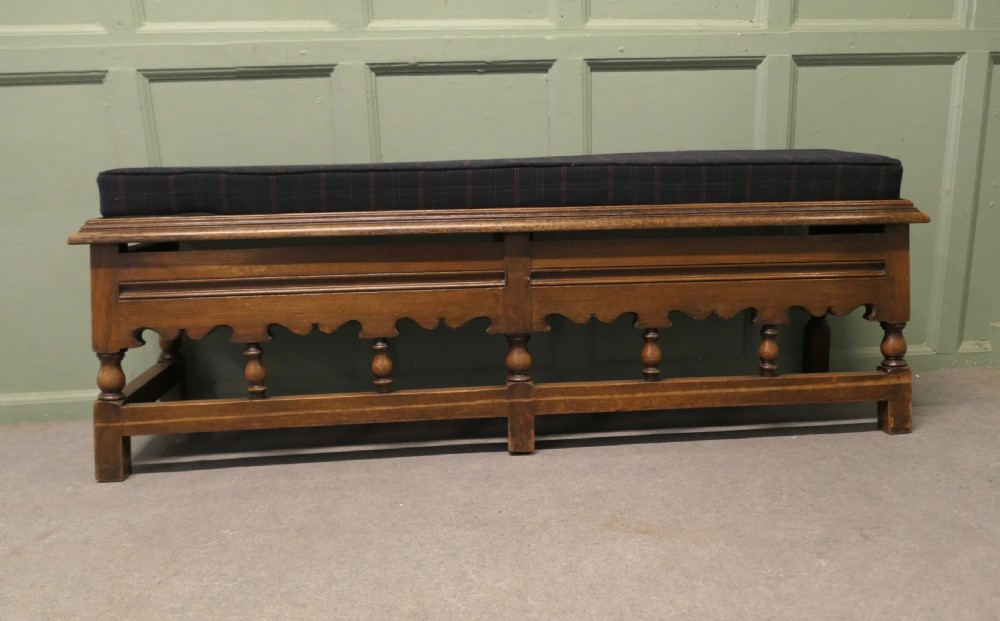 An antique brown oak hall bench featuring turned spindles, a scalloped apron, and a dark tartan tweed upholstered cushion top.