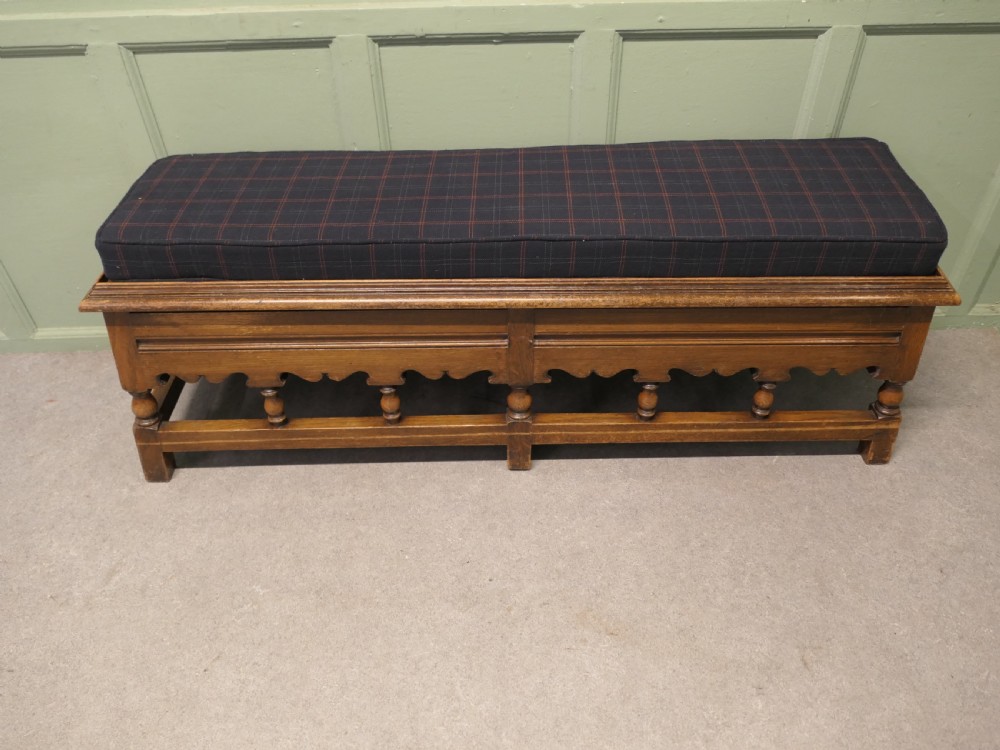 An antique brown oak hall bench featuring turned spindles, a scalloped apron, and a dark tartan tweed upholstered cushion top. View II