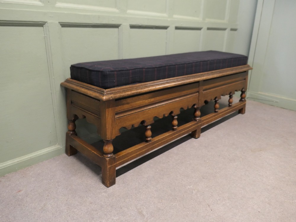 An antique brown oak hall bench featuring turned spindles, a scalloped apron, and a dark tartan tweed upholstered cushion top. View III