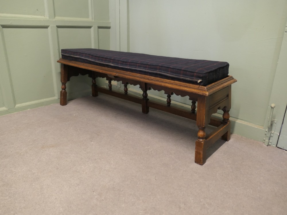 An antique brown oak hall bench featuring turned spindles, a scalloped apron, and a dark tartan tweed upholstered cushion top. View IV