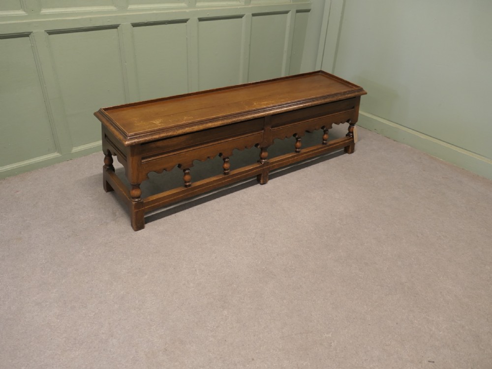 An antique brown oak hall bench featuring turned spindles, a scalloped apron, and a dark tartan tweed upholstered cushion top. View V