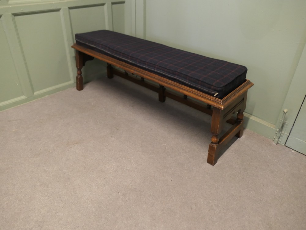 An antique brown oak hall bench featuring turned spindles, a scalloped apron, and a dark tartan tweed upholstered cushion top. View VI