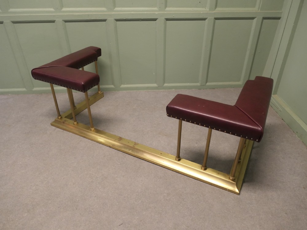 An Art Deco brass club fender featuring corner seats upholstered in burgundy leather with brass stud trimming, supported by vertical brass columns. View III