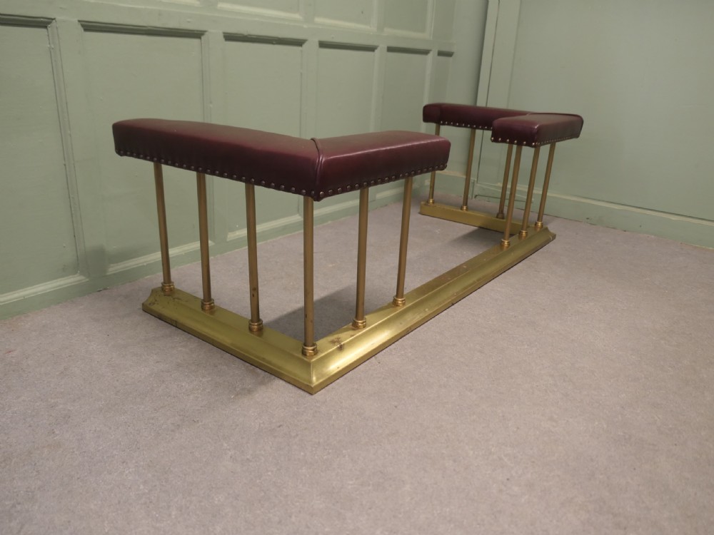 An Art Deco brass club fender featuring corner seats upholstered in burgundy leather with brass stud trimming, supported by vertical brass columns. View IV