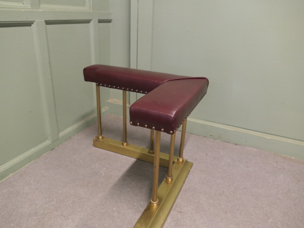 An Art Deco brass club fender featuring corner seats upholstered in burgundy leather with brass stud trimming, supported by vertical brass columns. View VI