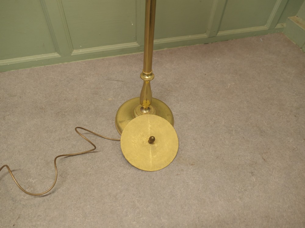 A slender turned brass floor lamp with a moulded circular base, topped with a cream patterned fabric shade featuring fringe trim. View VI