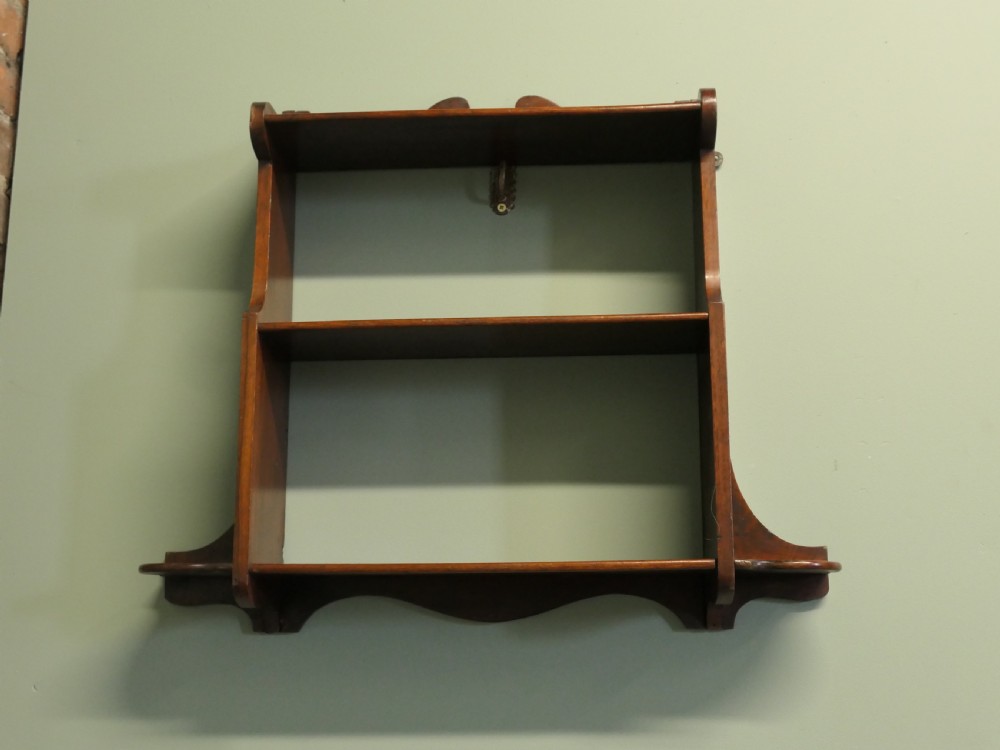 An antique dark brown wooden wall-hanging shelf unit with three open tiers and shaped decorative side panels.