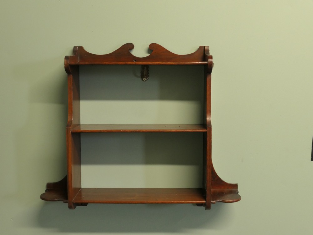 An antique dark brown wooden wall-hanging shelf unit with three open tiers and shaped decorative side panels. View II