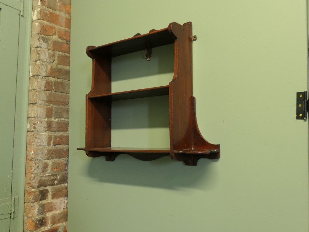 An antique dark brown wooden wall-hanging shelf unit with three open tiers and shaped decorative side panels. View III