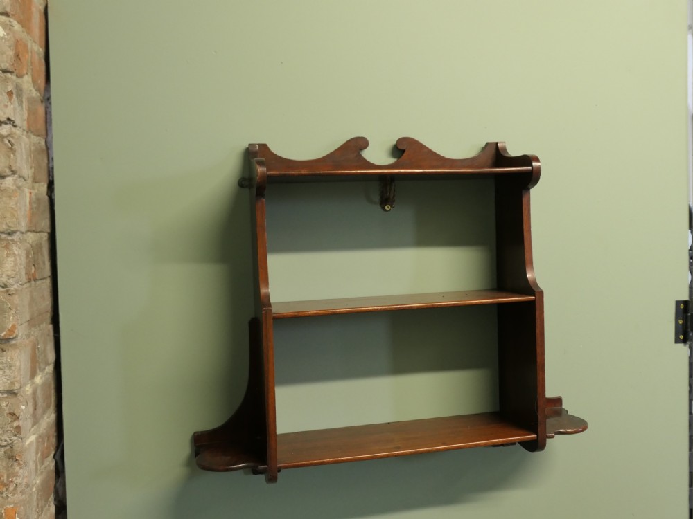 An antique dark brown wooden wall-hanging shelf unit with three open tiers and shaped decorative side panels. View IV