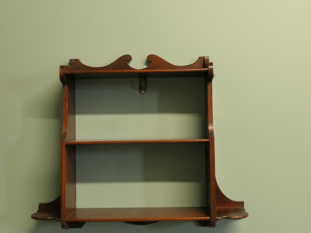 An antique dark brown wooden wall-hanging shelf unit with three open tiers and shaped decorative side panels. View V