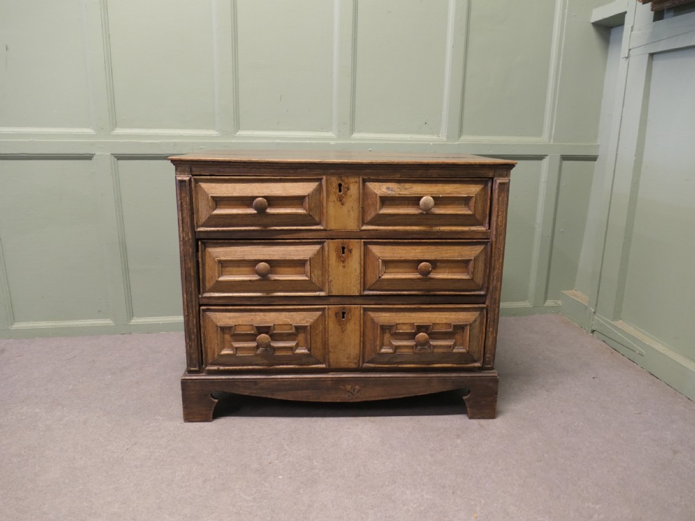 A seventeenth-century oak chest featuring three drawers with geometric moulded fronts, wooden turned knobs, and panelled sides. View III
