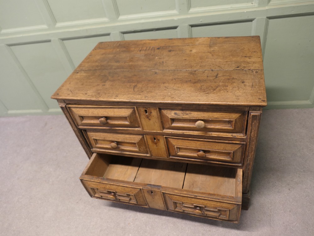 A seventeenth-century oak chest featuring three drawers with geometric moulded fronts, wooden turned knobs, and panelled sides. View IV