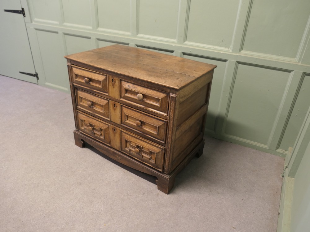 A seventeenth-century oak chest featuring three drawers with geometric moulded fronts, wooden turned knobs, and panelled sides. View V