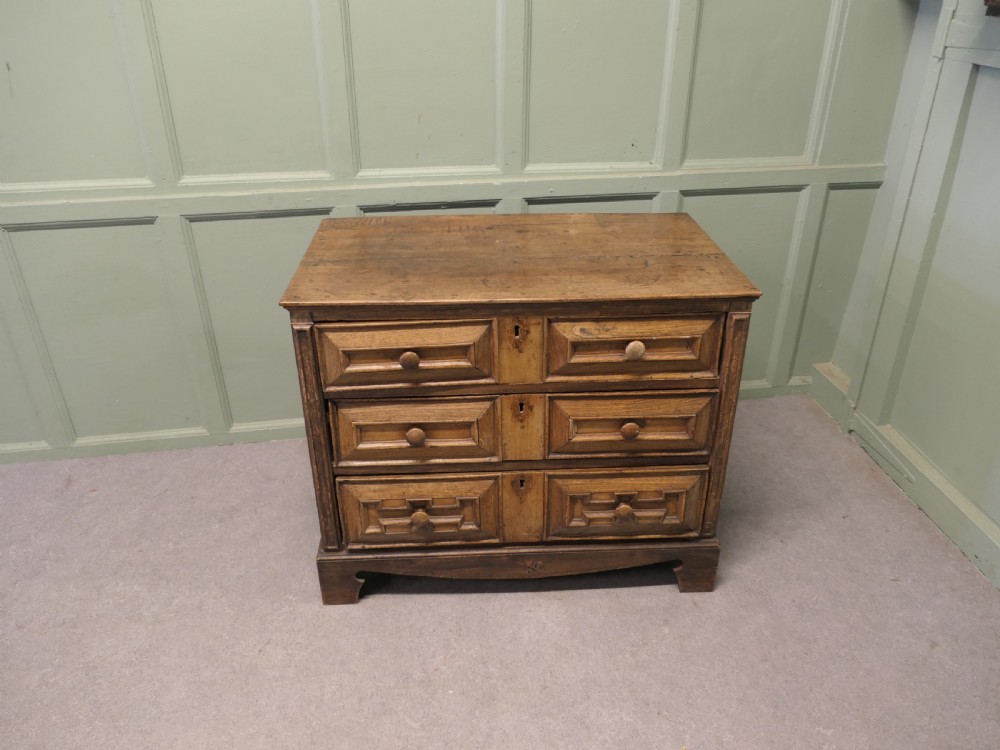 A seventeenth-century oak chest featuring three drawers with geometric moulded fronts, wooden turned knobs, and panelled sides. View VI