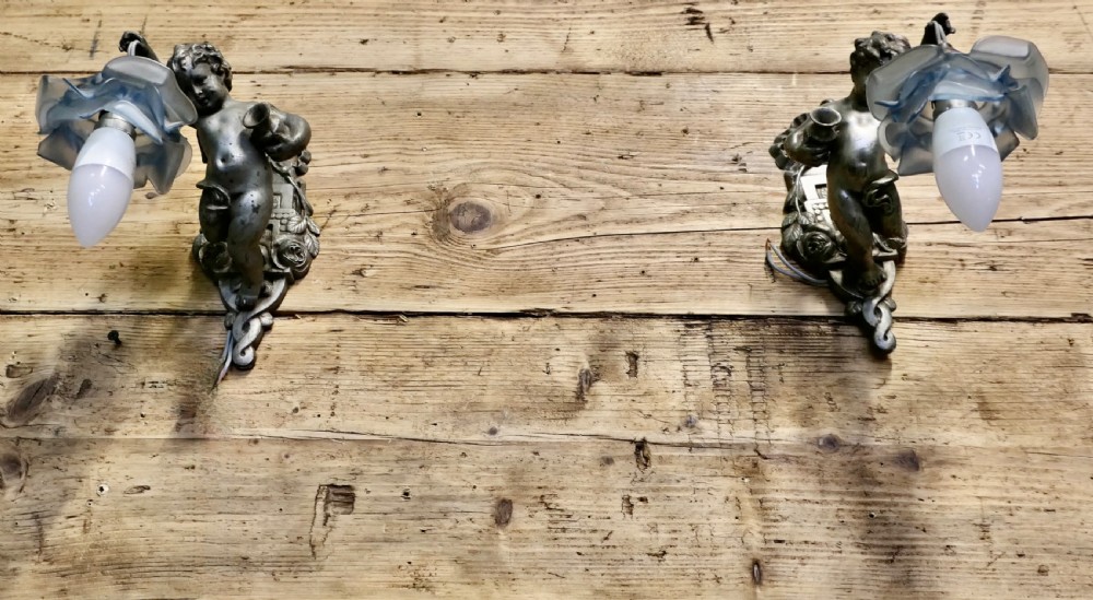 A pair of cast metal wall sconces shaped as figurative cherubs supporting soft blue flower-formed glass shades.