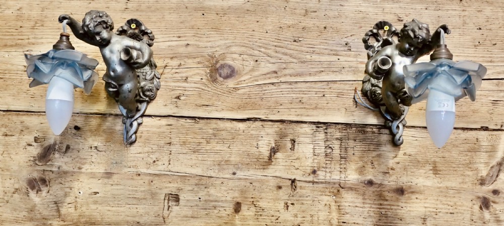 A pair of cast metal wall sconces shaped as figurative cherubs supporting soft blue flower-formed glass shades. View III
