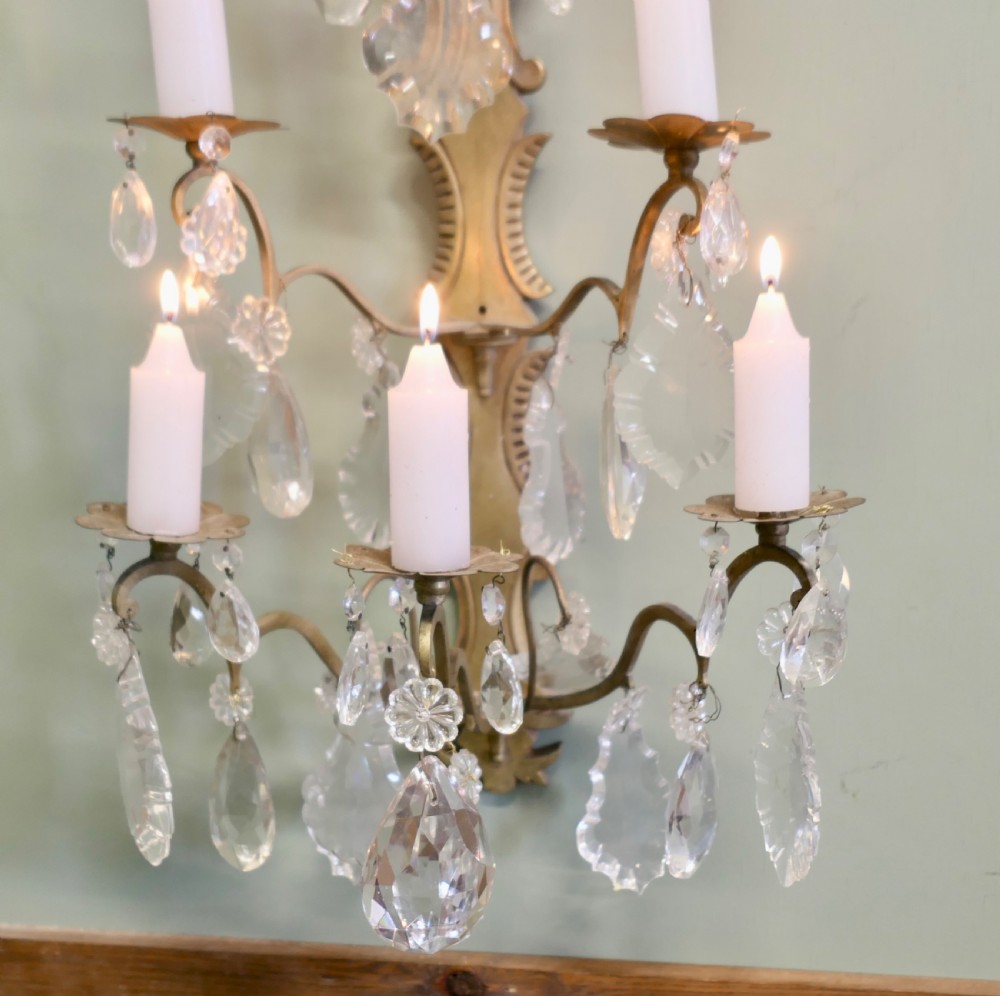 A 19th-century French brass wall sconce candelabra featuring four candle holders and clear crystal glass droplets. View IV