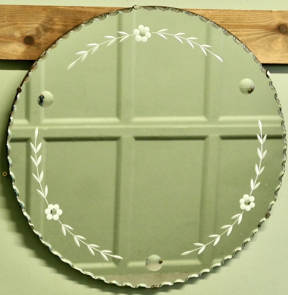 A circular frameless glass wall mirror featuring etched floral garlands along the inner border and a scalloped outer rim.