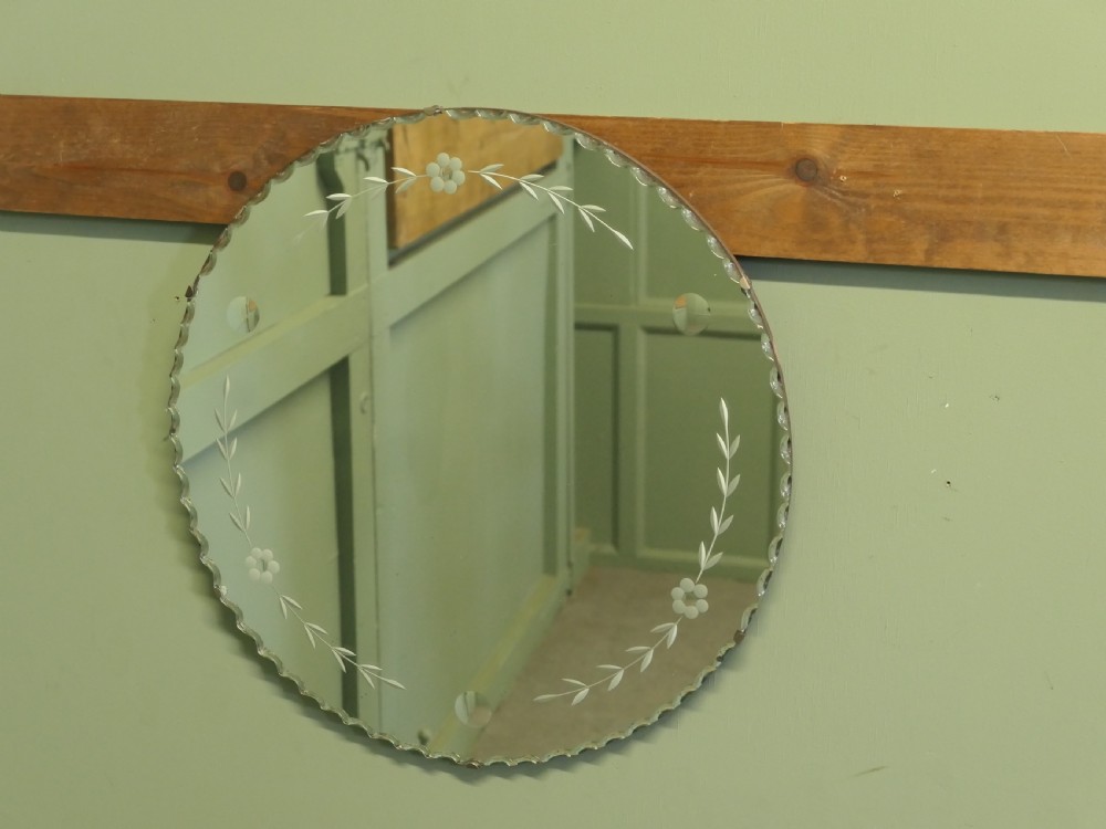 A circular frameless glass wall mirror featuring etched floral garlands along the inner border and a scalloped outer rim. View II