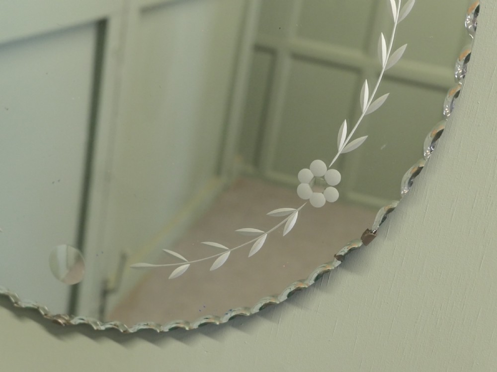 A circular frameless glass wall mirror featuring etched floral garlands along the inner border and a scalloped outer rim. View IV