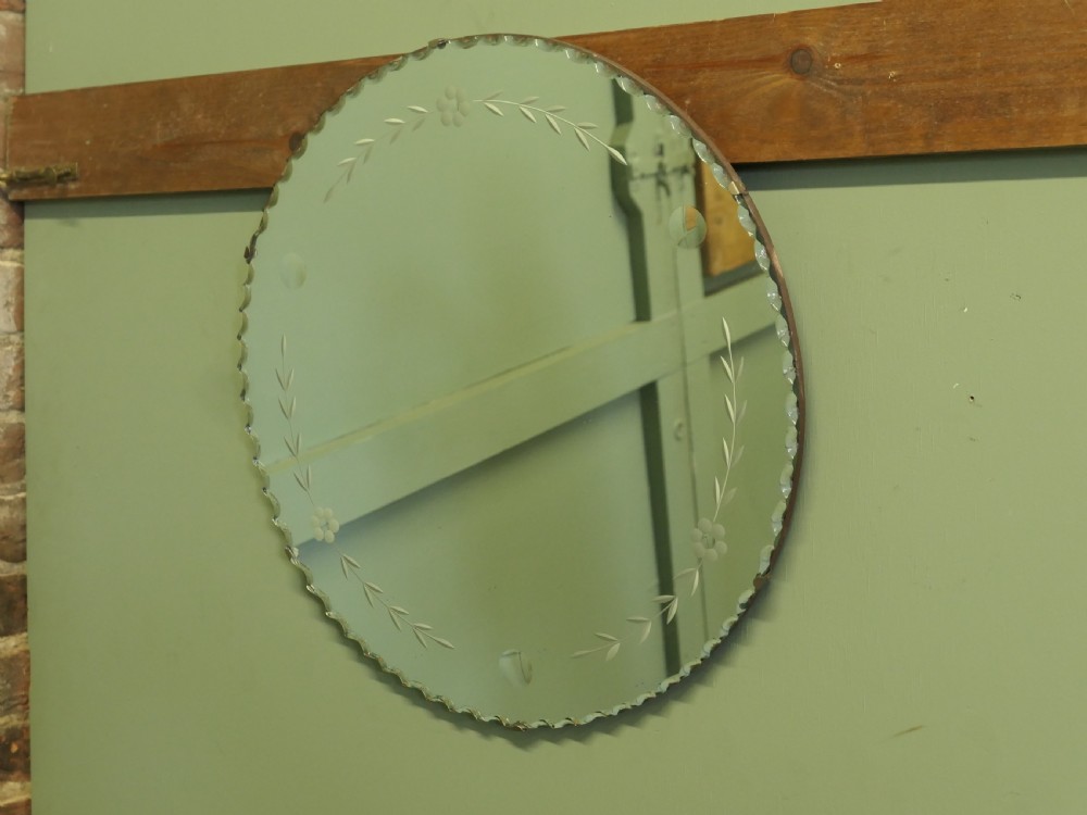 A circular frameless glass wall mirror featuring etched floral garlands along the inner border and a scalloped outer rim. View V