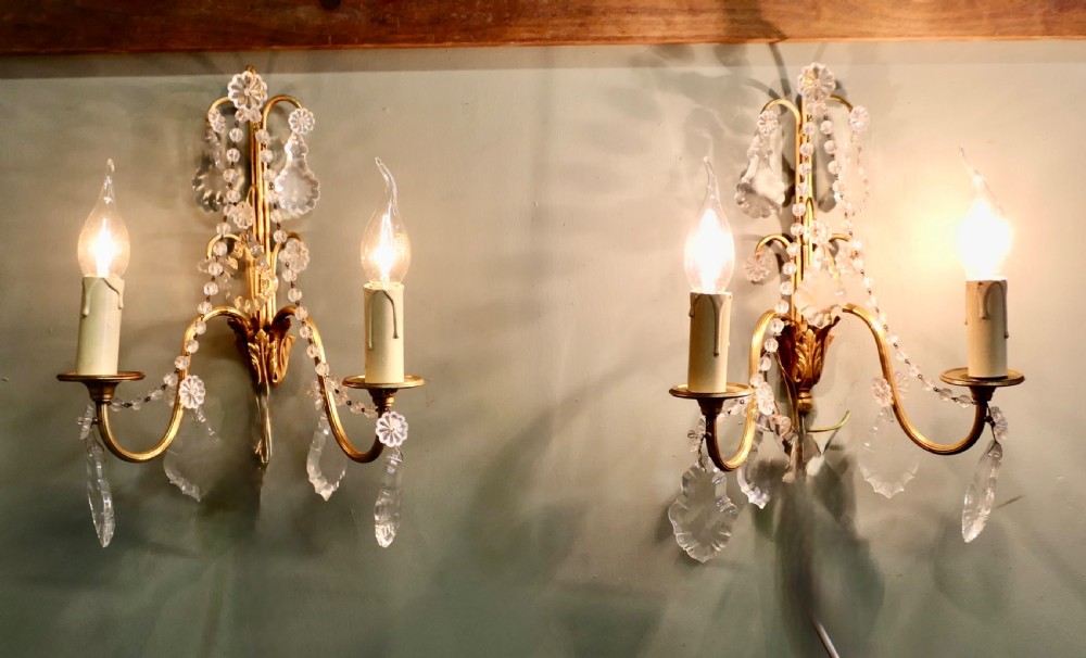 A pair of twin-arm gilt brass French wall sconces decorated with crystal garlands, faceted drops, and candle-effect fittings.