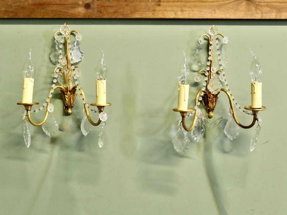 A pair of twin-arm gilt brass French wall sconces decorated with crystal garlands, faceted drops, and candle-effect fittings. View II