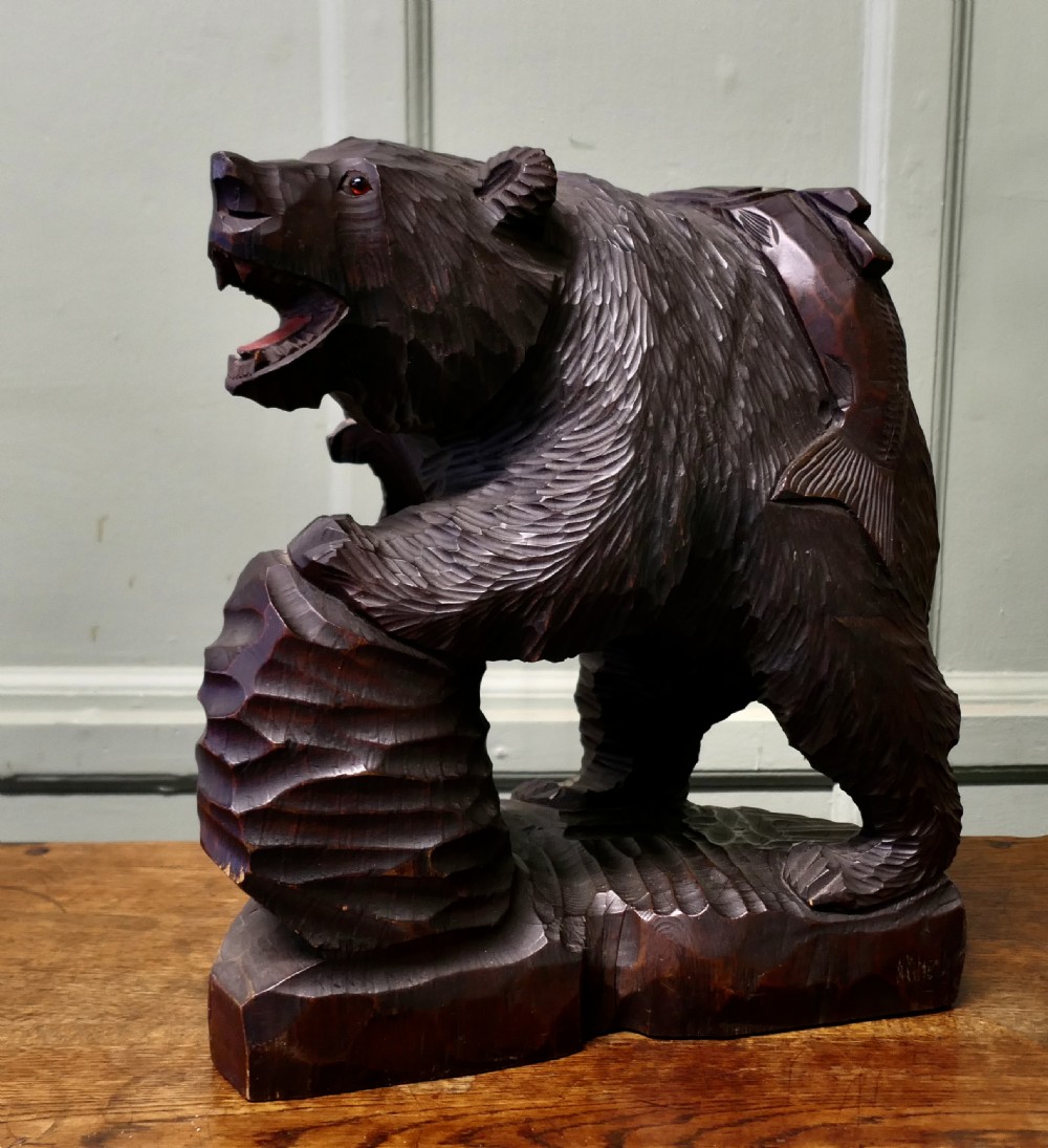 A hand-carved dark linden wood bear sculpture depicting a standing roaring bear holding a fish.