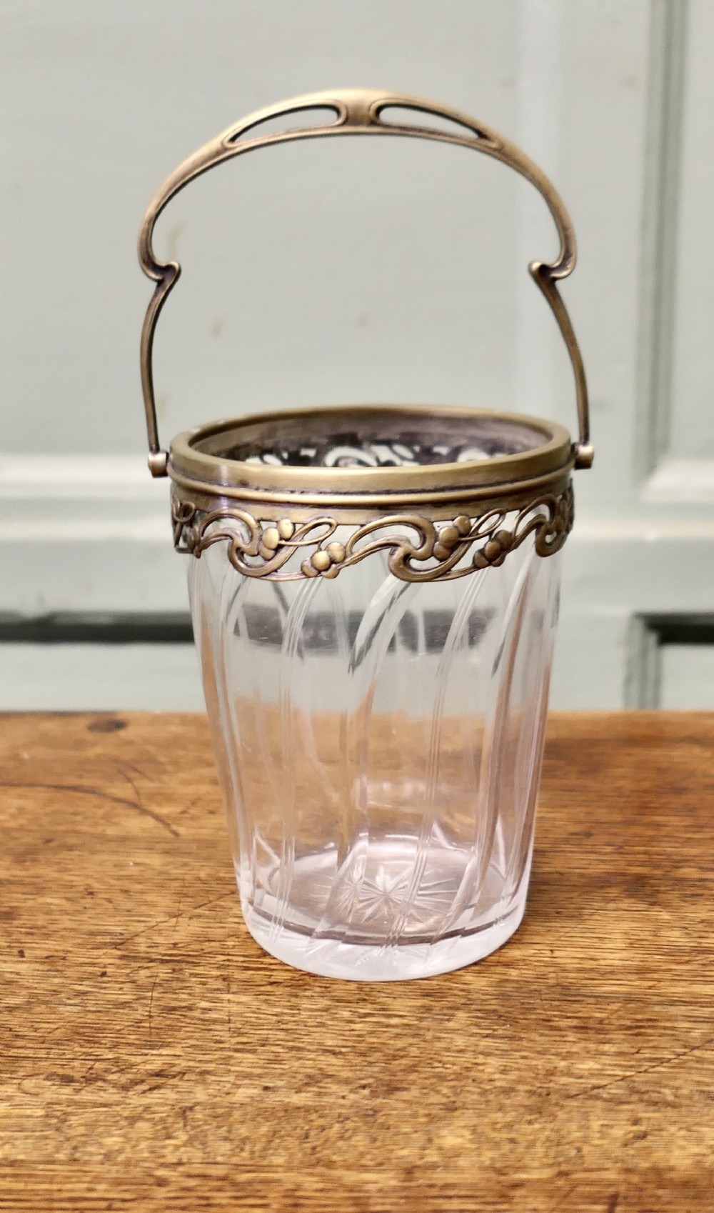 A small French Art Nouveau clear glass personal ice bucket featuring spiral fluted sides and an ornate brass collar with a swing handle.