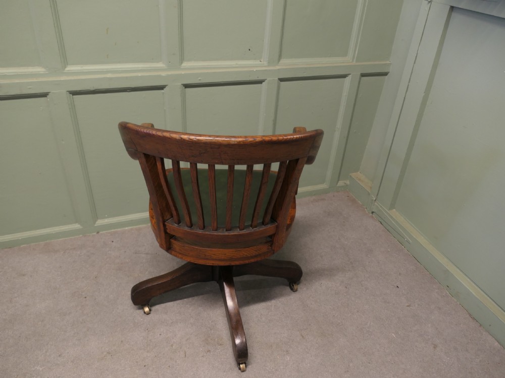 An Art Deco oak swivel desk chair featuring a curved backrest with vertical slats, a green leather padded seat, and a quadruped base on castors. View IV