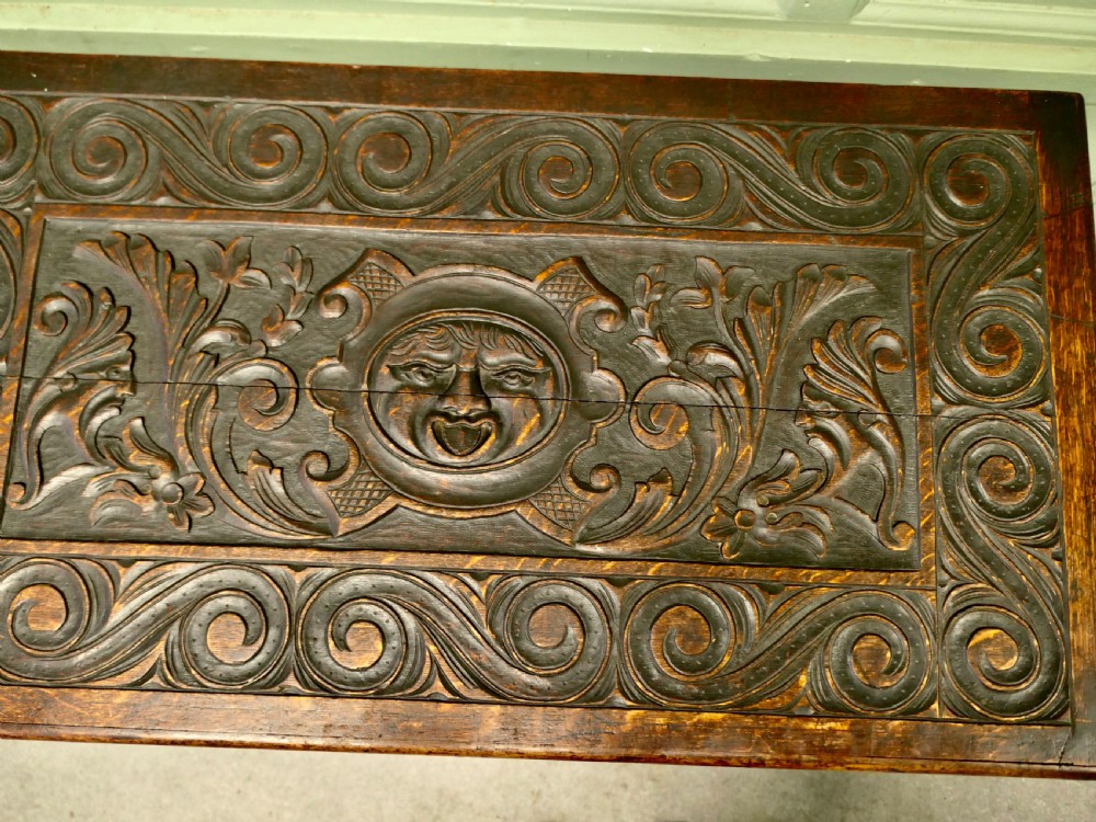 A dark carved oak mule chest featuring a hinged lid, relief-carved scrollwork and geometric patterns, and two drawers at the bottom with brass drop handles. View III