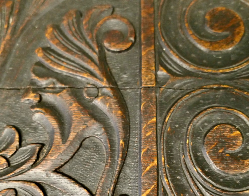 A dark carved oak mule chest featuring a hinged lid, relief-carved scrollwork and geometric patterns, and two drawers at the bottom with brass drop handles. View IV