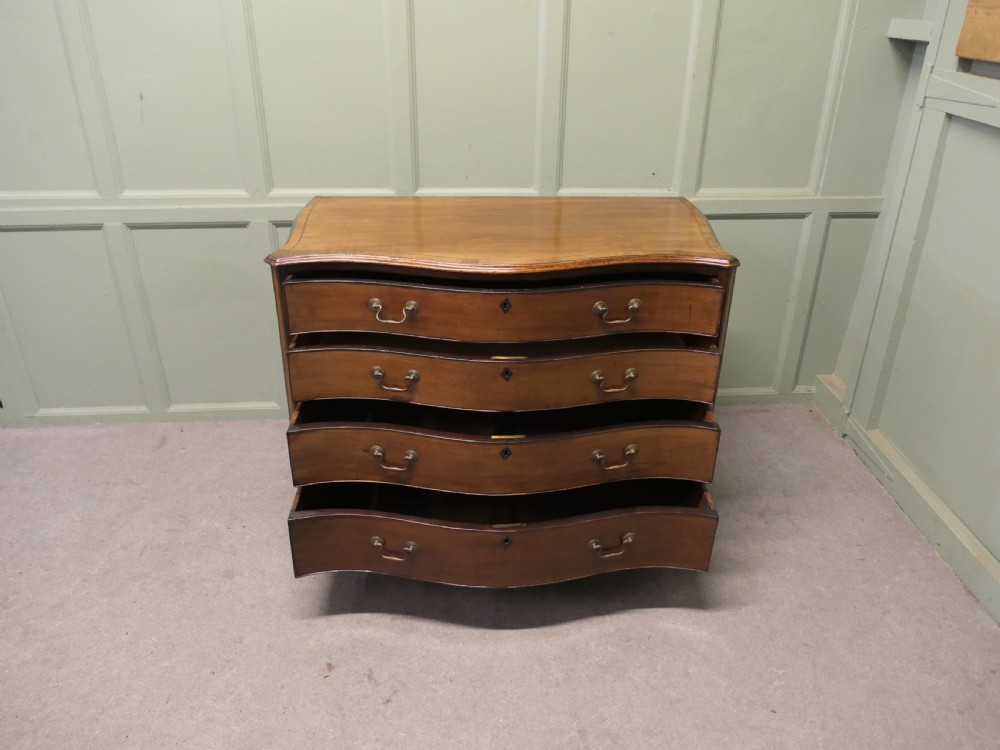 A Georgian serpentine-fronted walnut chest of drawers featuring four graduated drawers with brass swan-neck handles. View V
