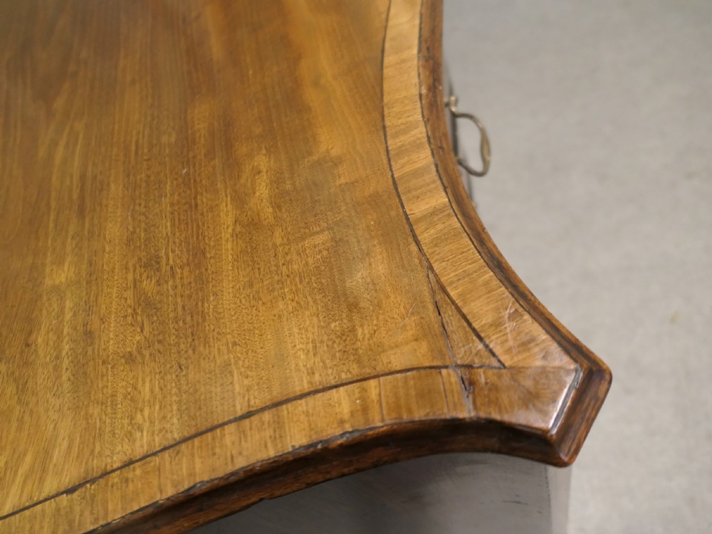 A Georgian serpentine-fronted walnut chest of drawers featuring four graduated drawers with brass swan-neck handles. View VI