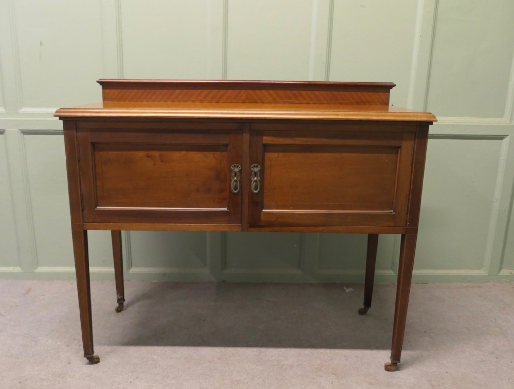 A late Victorian warm brown walnut side cupboard featuring twin panelled doors, a low gallery back with parquetry inlay, and square tapered legs on brass castors. View III