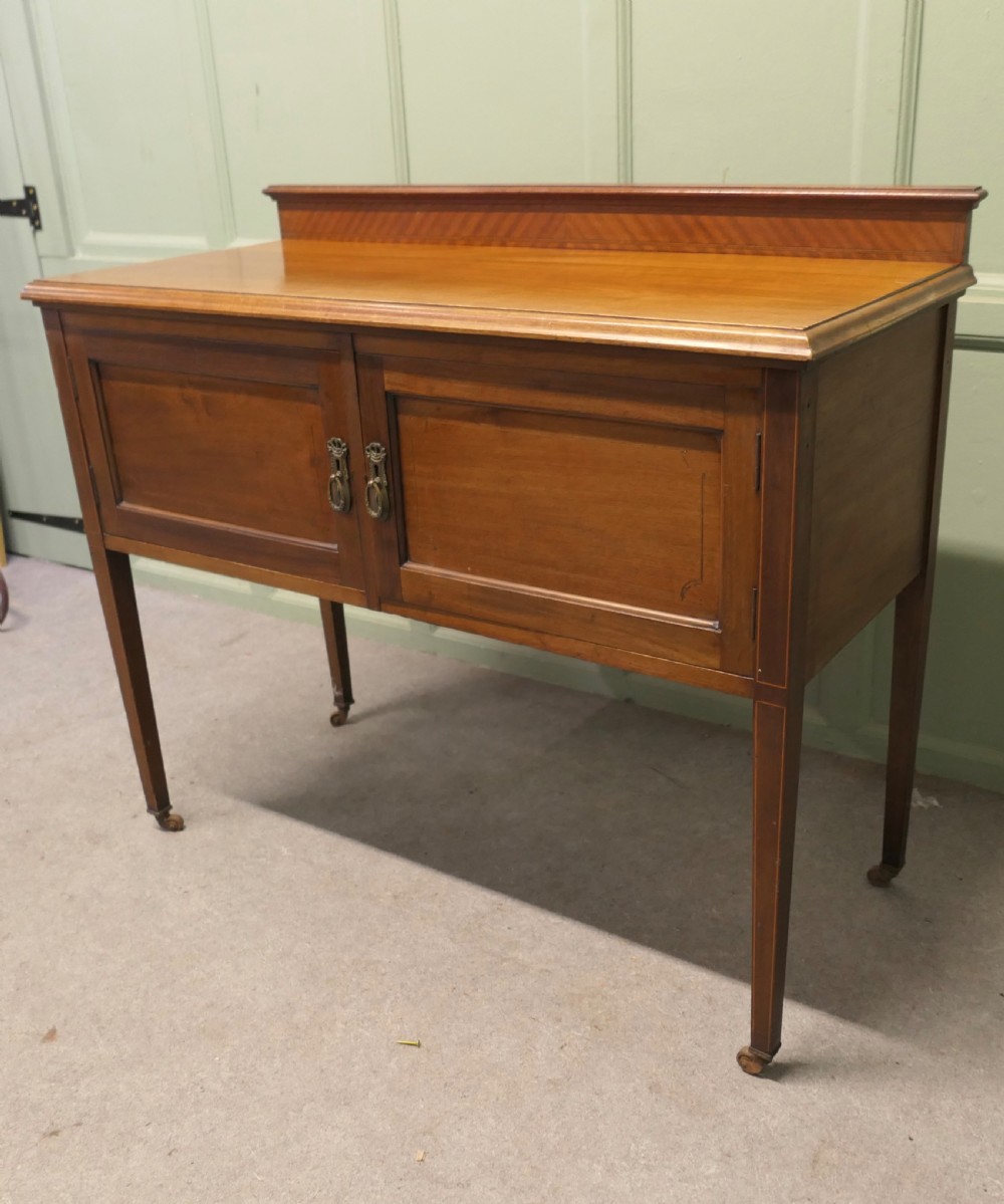 A late Victorian warm brown walnut side cupboard featuring twin panelled doors, a low gallery back with parquetry inlay, and square tapered legs on brass castors. View IV