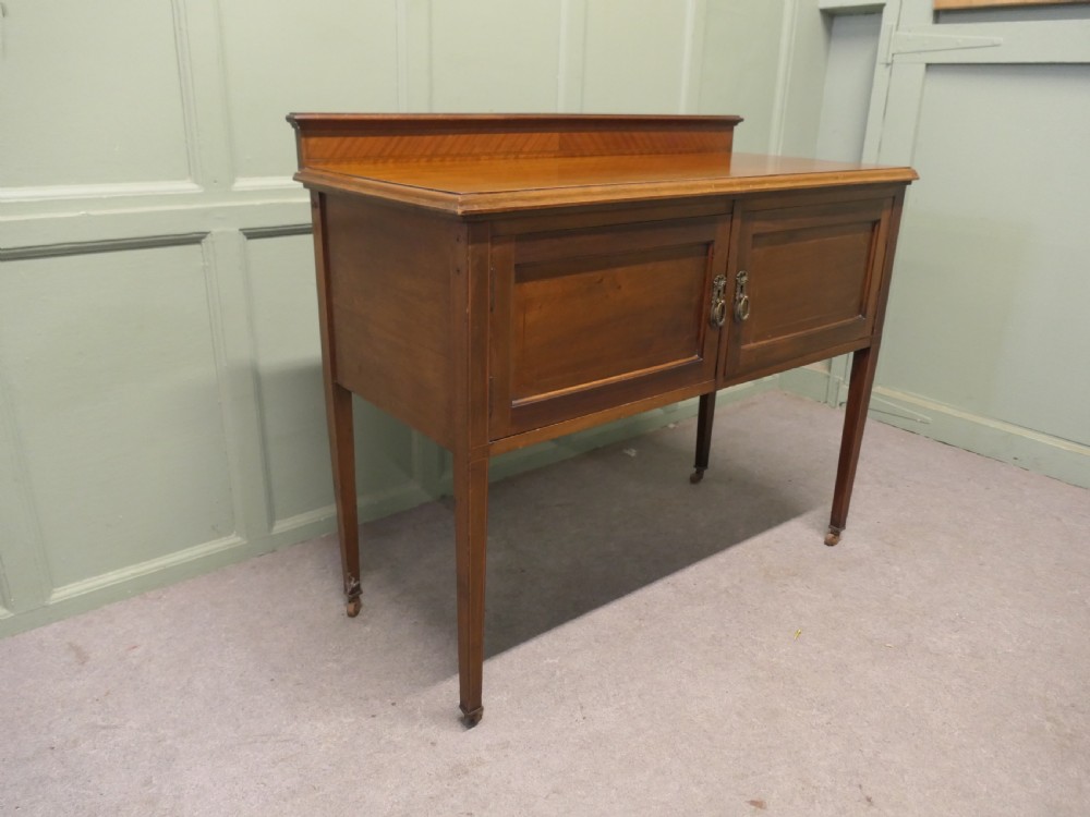 A late Victorian warm brown walnut side cupboard featuring twin panelled doors, a low gallery back with parquetry inlay, and square tapered legs on brass castors. View VI