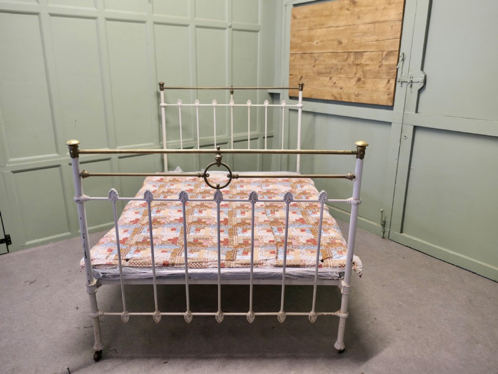 A Victorian off-white painted cast iron double bedstead featuring brass top rails, brass finials, and a central circular motif.