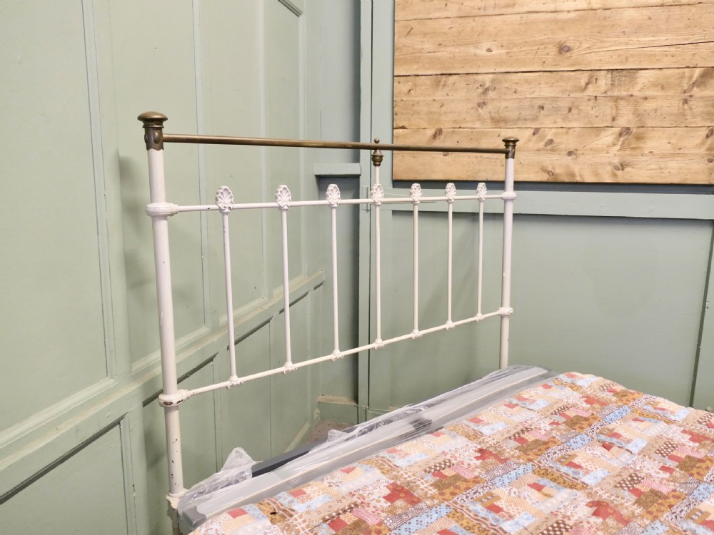 A Victorian off-white painted cast iron double bedstead featuring brass top rails, brass finials, and a central circular motif. View III