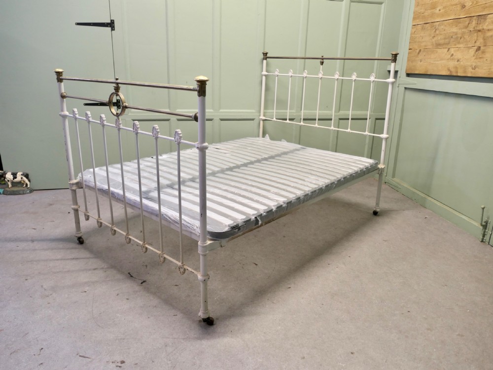 A Victorian off-white painted cast iron double bedstead featuring brass top rails, brass finials, and a central circular motif. View IV