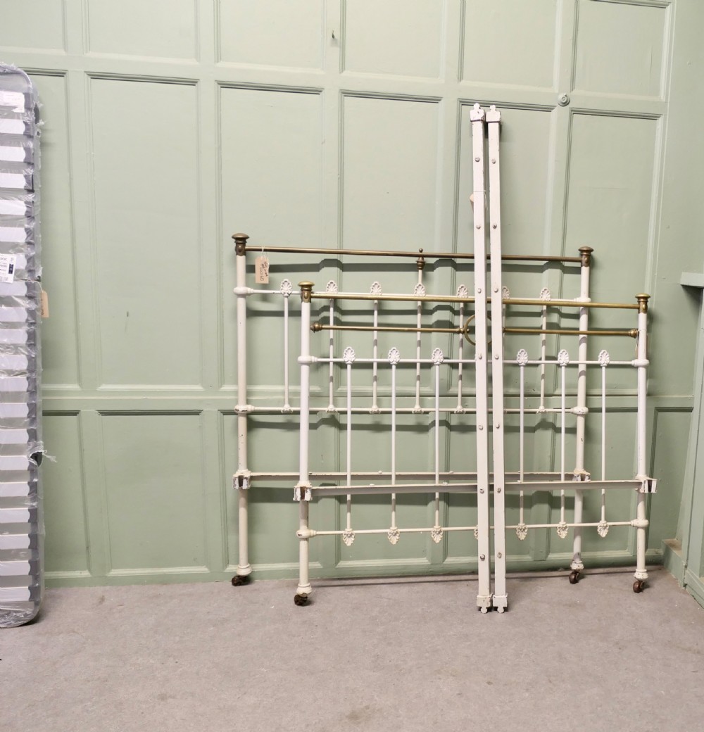 A Victorian off-white painted cast iron double bedstead featuring brass top rails, brass finials, and a central circular motif. View V