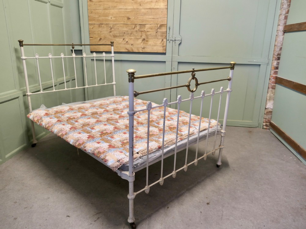 A Victorian off-white painted cast iron double bedstead featuring brass top rails, brass finials, and a central circular motif. View VI