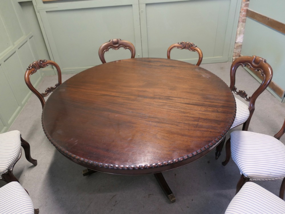 A circular dark mahogany dining table surrounded by eight matching carved balloon-back dining chairs with blue and white striped fabric seats. View II