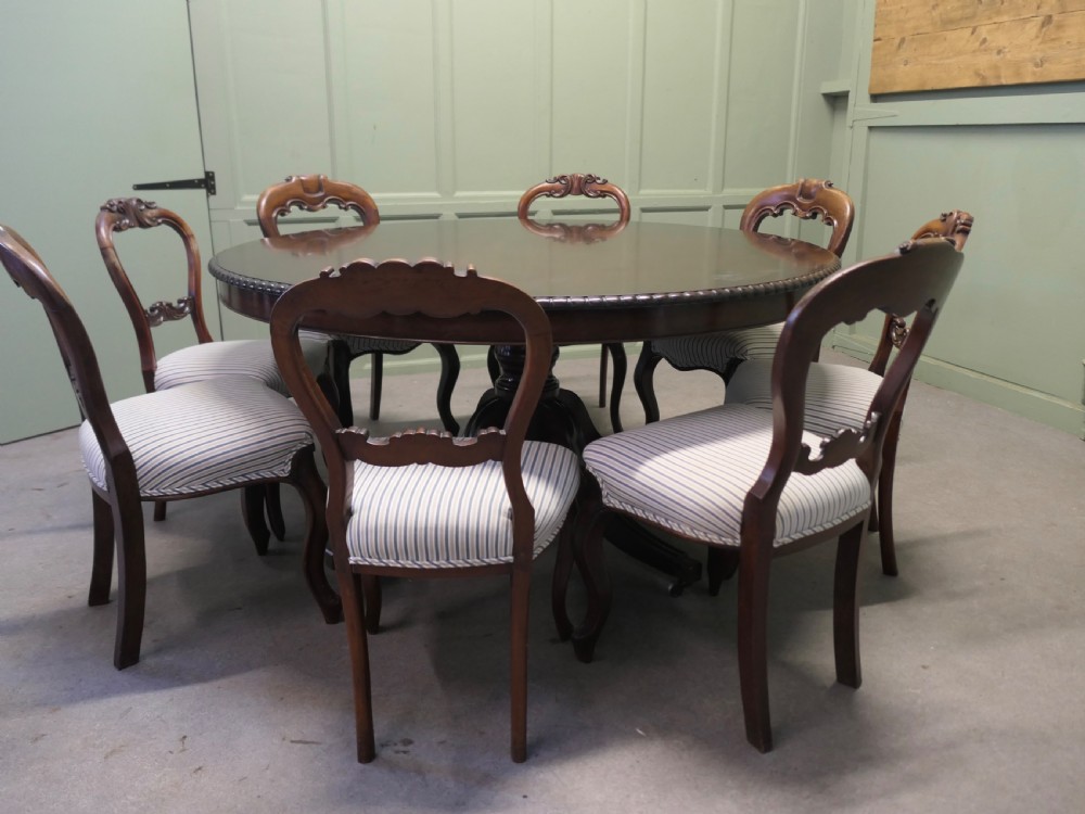 A circular dark mahogany dining table surrounded by eight matching carved balloon-back dining chairs with blue and white striped fabric seats. View III