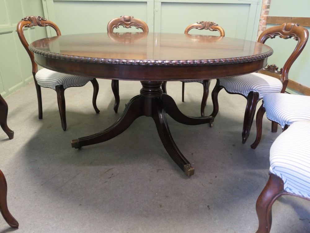 A circular dark mahogany dining table surrounded by eight matching carved balloon-back dining chairs with blue and white striped fabric seats. View V