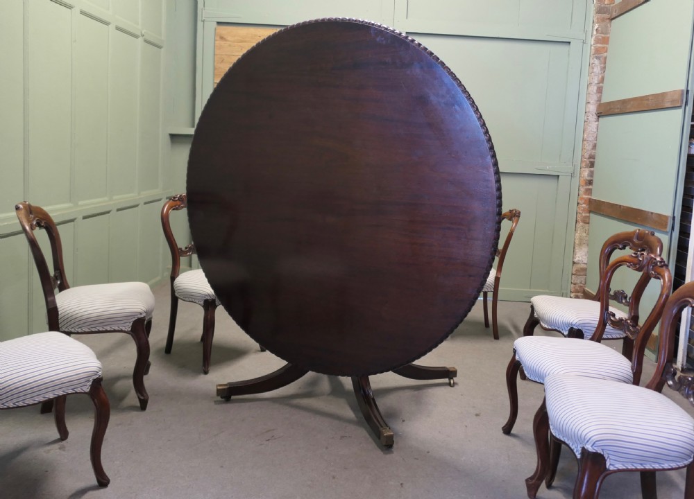 A circular dark mahogany dining table surrounded by eight matching carved balloon-back dining chairs with blue and white striped fabric seats. View VI