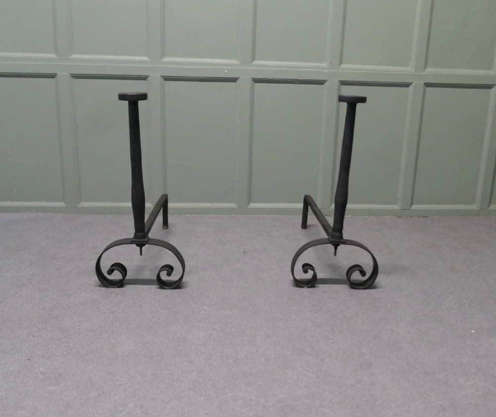 A pair of tall dark iron andirons featuring scrolled pedestal bases and vertical upright pillars with flat caps.